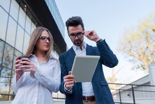 Businessman and businesswoman standing in the street looking on digital tablet